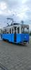 Stary niebieski tramwaj stojący na placu przed zajezdnią. Plac wyłożony jest kostką brukową.