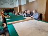 Trzynastu starszych mężczyzn i kobiet siedzi przy długim stole nakrytym zielonym obrusem w sali konferencyjnej archiwum. Na stole leży duża mapa. Seniorzy słuchają wykładu. Trzy osoby mają przed sobą stary poszyt akt i oglądają go z zaciekawieniem.