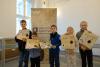 Trzech chłopców i dwie dziewczynki stoją na sali wystawowej archiwum na tle banera z napisem Archiwa Państwowe Archiwum Państwowe we Wrocławiu. Trzymają w dłoniach swoje własnoręcznie wykonane dokumenty. Pozują do wspólnego zdjęcia z uśmiechem prezentując swoje prace.