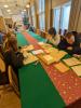 Dwie grupy studentów siedzących w sali konferencyjnej przy stole nakrytym zielonym obrusem. Na stole leżą dokumenty. Studenci przeglądają stare dokumenty.