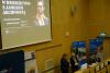 Duża sala konferencyjna w układzie amfiteatralnym. Dwie kobiety prowadzą wykład prezentujący grę planszową. Za nimi na dużym ekranie wyświetlona prezentacja zatytułowana "Graj w dziedzictwo z Jamesem Archiwistą".