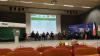 Duża sala konferencyjna z krzesłami w kolorze czerwonym. Na scenie grupa osób w wojskowych mundurach, dyrektorzy i oficjele. Na środku duży ekran z wyświetloną prezentacją multimedialną i programem spotkania.