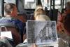 Wnętrze autobusu, obiektyw zwrócony w kierunku przodu pojazdu. Czyjaś ręka trzyma duże, poziome, czarno-białe zdjęcie, które przedstawia dawną wrocławską ulicę, budynki rozciągające się wzdłuż niej oraz przechodniów. W autobusie widoczne są trzy rzędy podwójnych miejsc, na których siedzą dorosłe osoby.