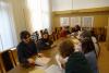 Sala konferencyjna. Studenci w dwóch grupach po pięć osób siedzą przy stole i przeglądają teczki z dokumentami.