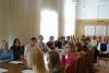 Grupa trzynastu studentek, studentów i profesor siedzą w sali konferencyjnej przy długim stole. Słuchają wykładu.